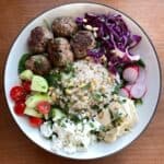 bowl with lamb meatballs, Israeli couscous, hummus, vegetables, and pine nuts.