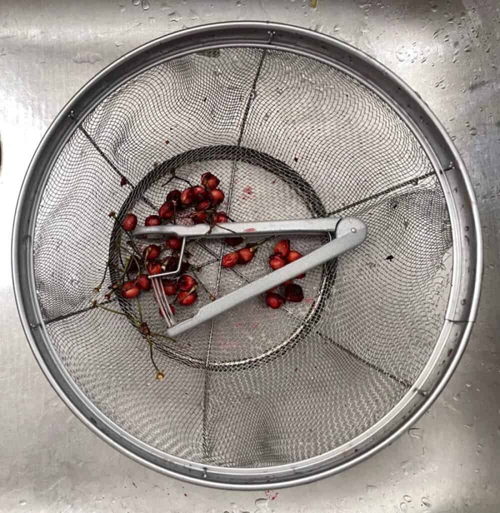 cherry pitter and pits in a colander in the sink
