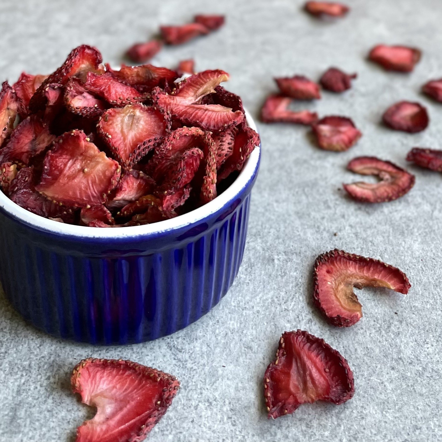dehydrated strawberry chips in a bowl and scattered on a counter.