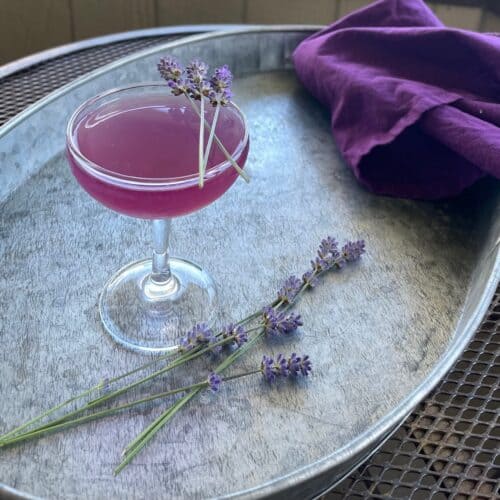 a purple cocktail on a tray with a purple napkin and several lavender sprigs
