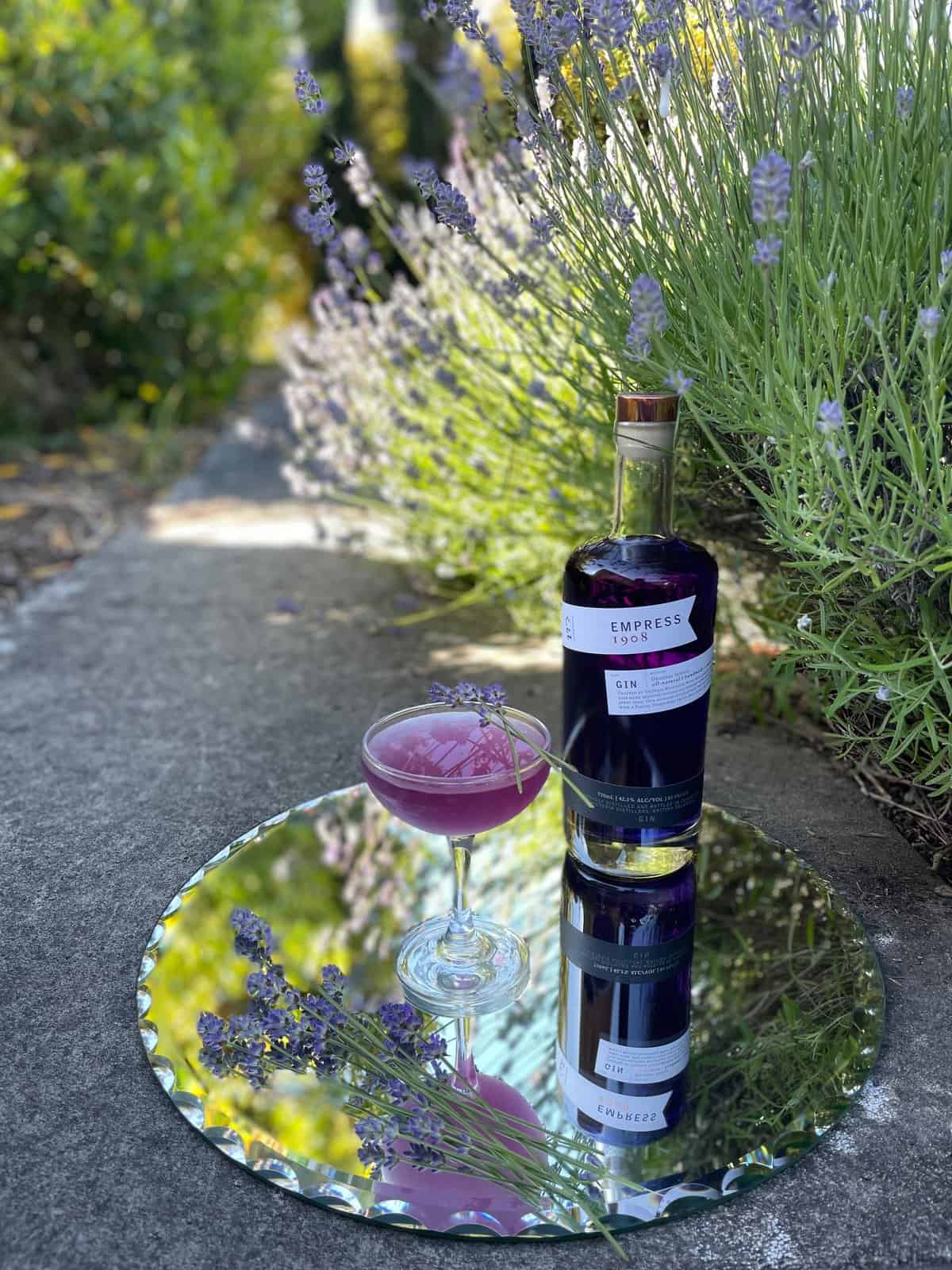 bottle and purple Empress gin cocktail on a mirrored tray with lavender sprigs.