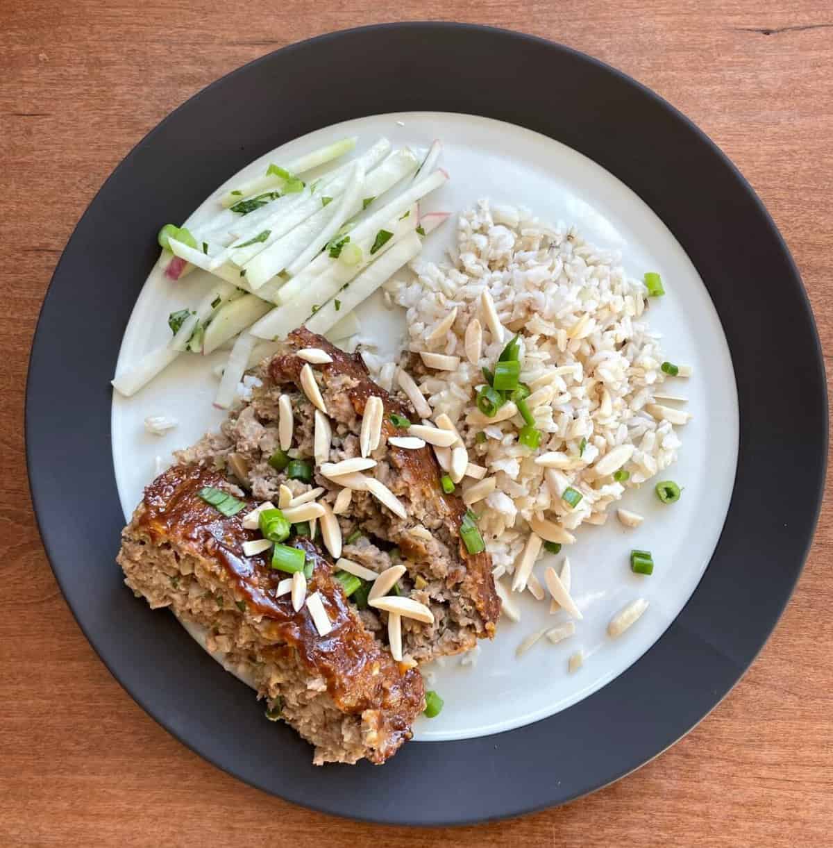 sliced duck meatloaf garnished with almonds, some rice, and kohlrabi coleslaw.