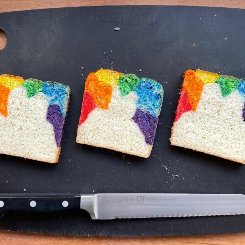 three slices of rainbow colored bread on a cutting board with a knife.