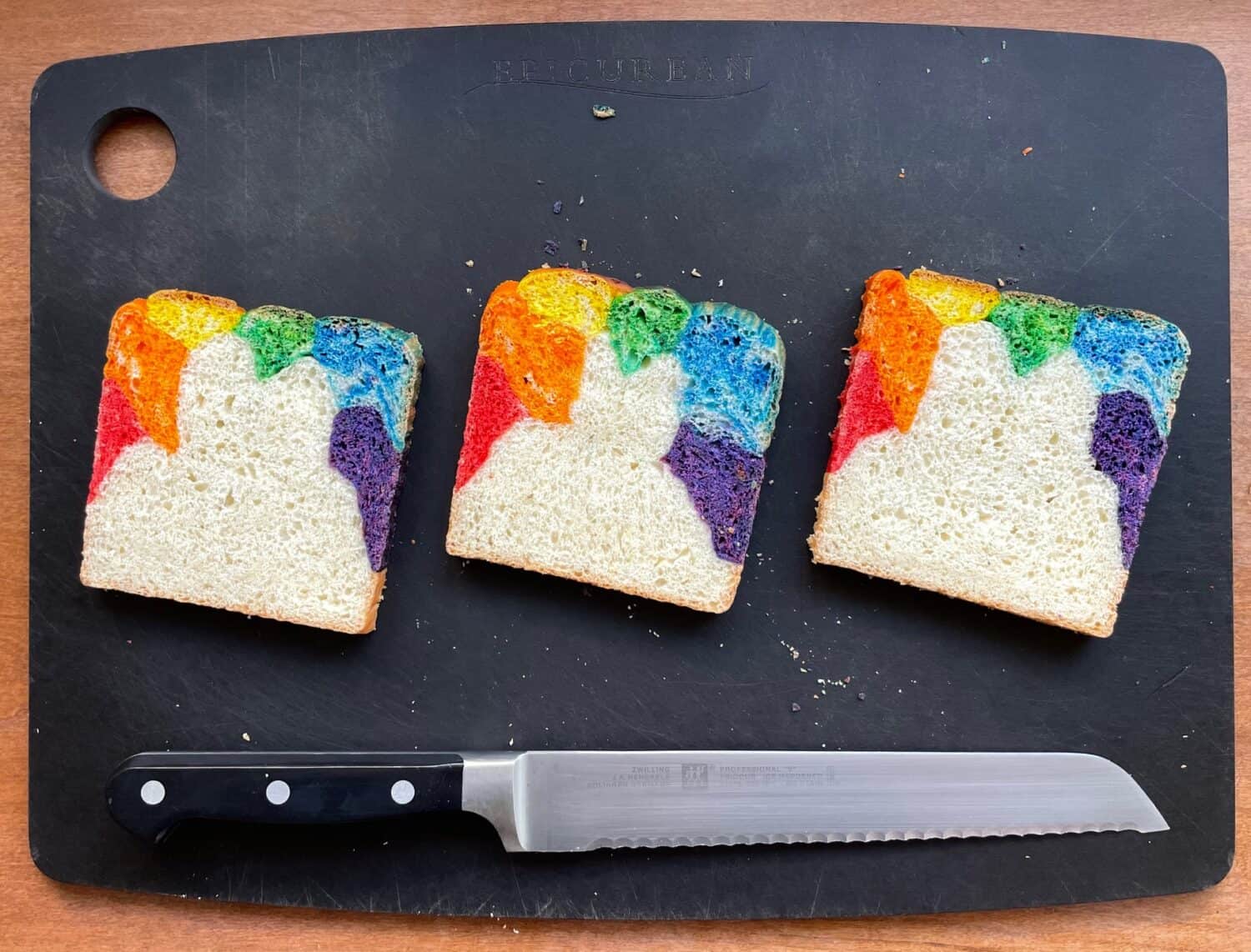 three slices of rainbow bread on a cutting board with a knife.