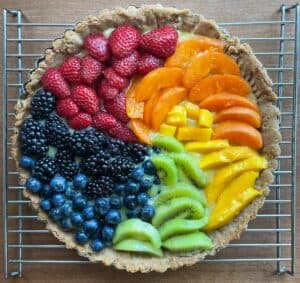 A rainbow fruit tart with strawberries, apricot, mango, kiwi, blueberries, and blackberries in a spiral pattern.