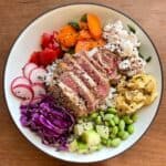 A rainbow poke bowl with sliced seared tuna, sushi crab salad, japanese scrambled eggs, and a rainbow colored array of vegetables.