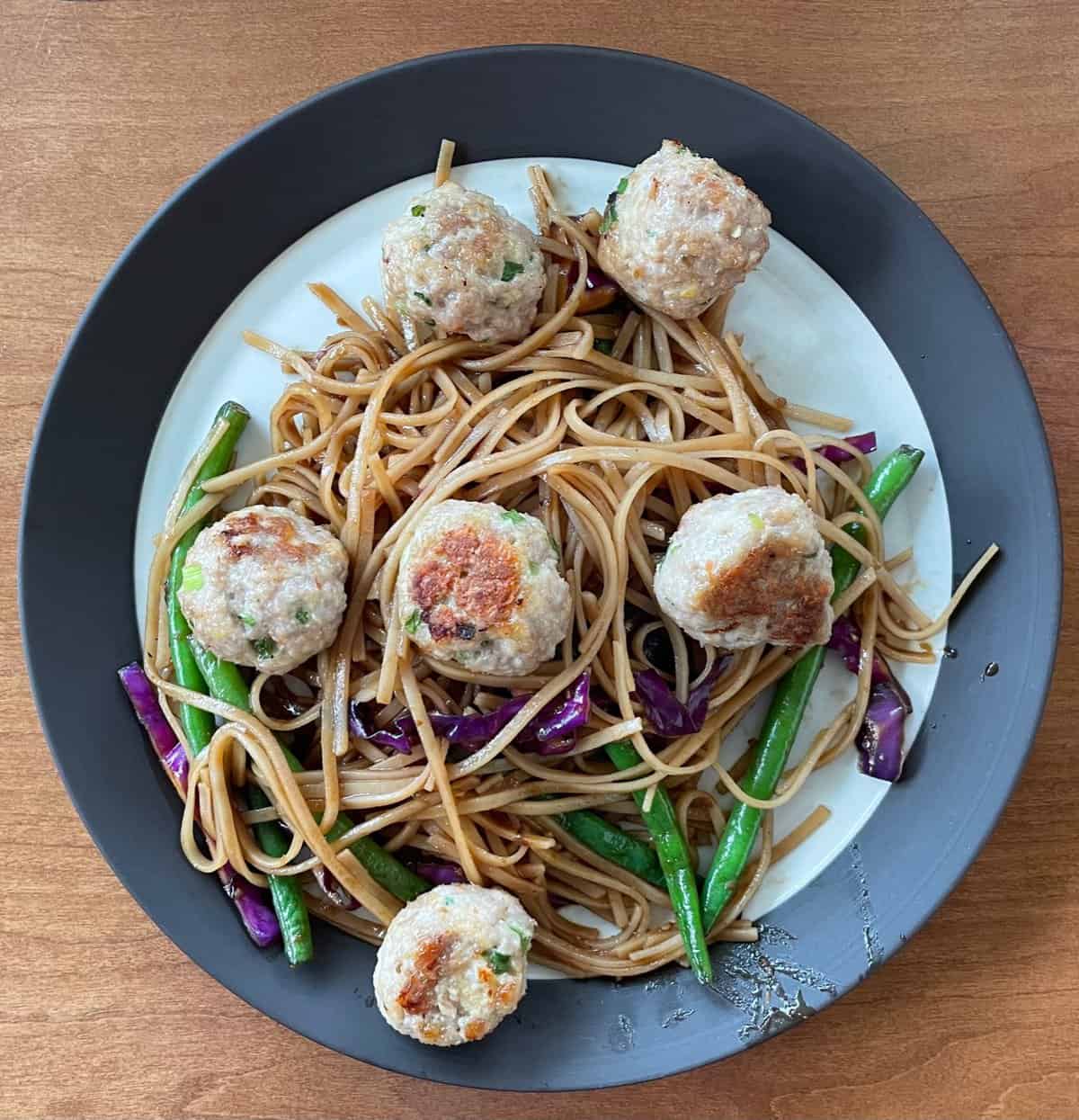 Shrimp and pork meatballs on a plate of noodles, green beans, and cabbage.