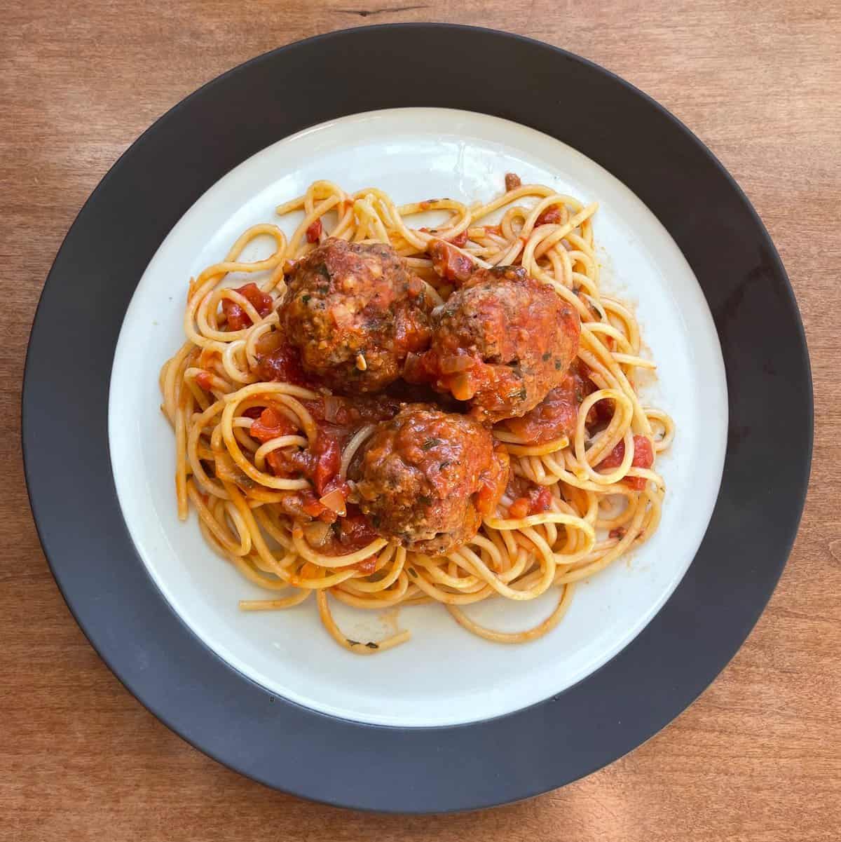 A plate of spaghetti with three braised meatballs in tomato sauce.