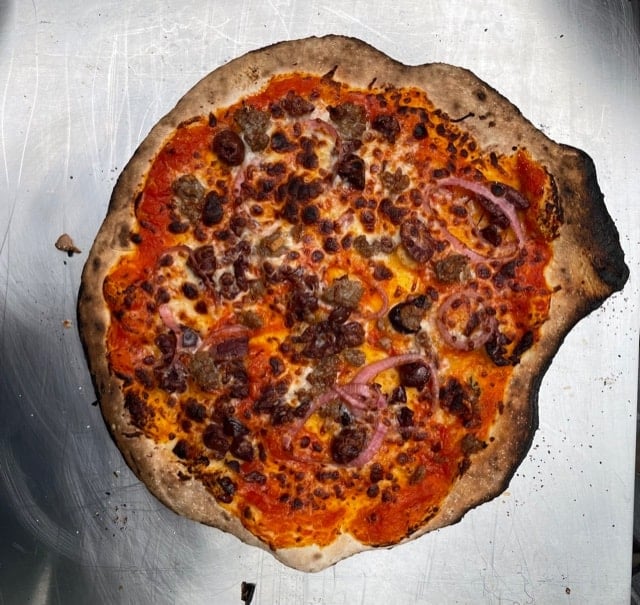 pizza with sausage and red onions burnt in the Ooni pizza oven.