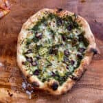 olive and artichoke pizza with pesto base cooked on ooni pizza dough.
