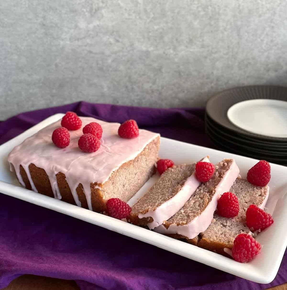 the summer raspberry cake recipe on a plate with a few slices and fresh raspberries.