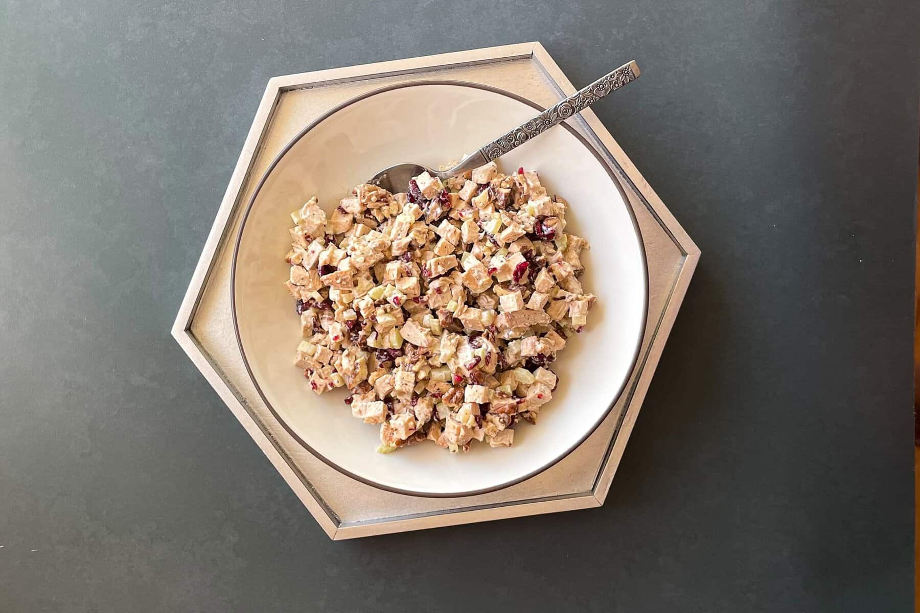 bowl of chicken salad with cranberries, pecans, and chopped celery and a metal spoon.