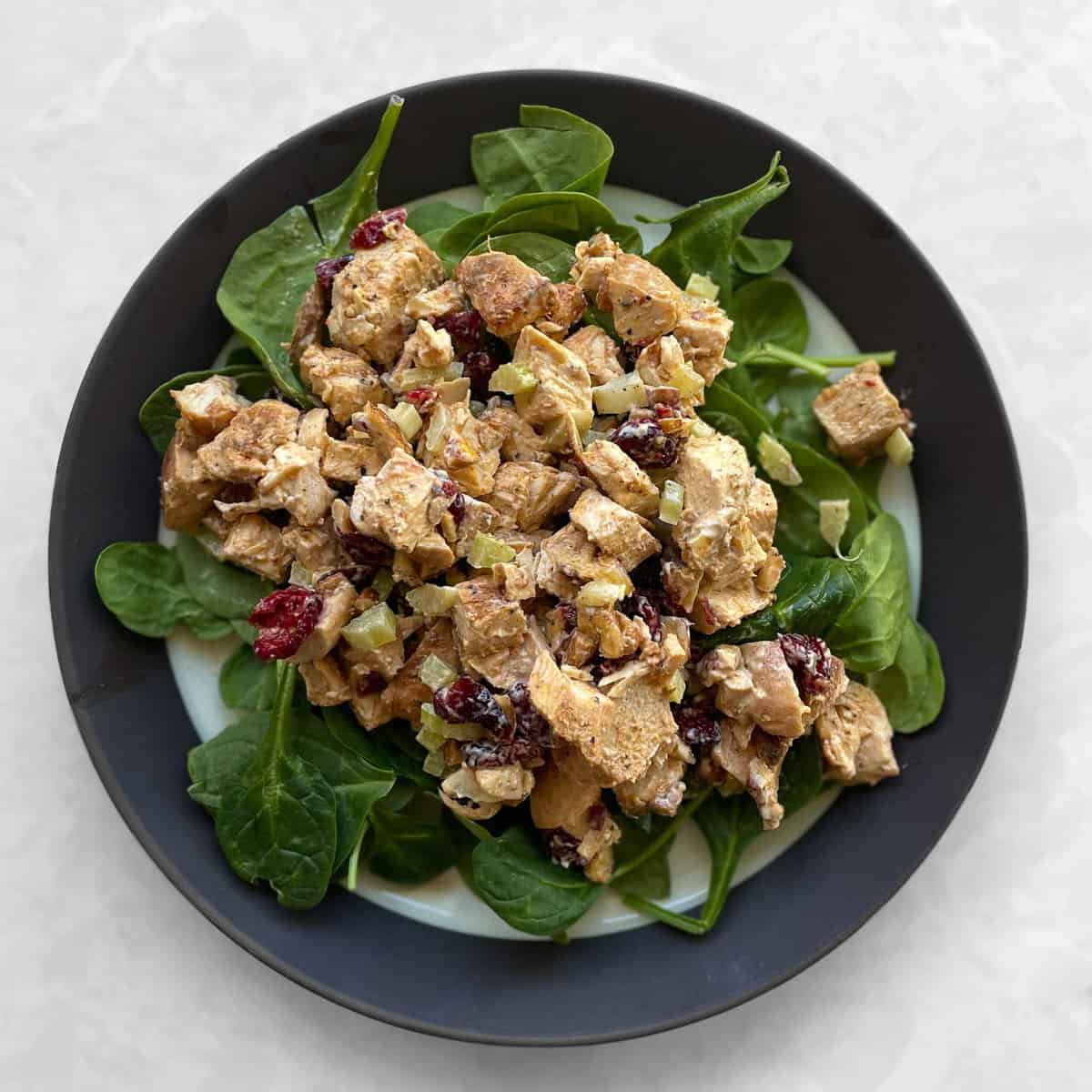 cranberry pecan chicken salad on a plate of baby spinach.