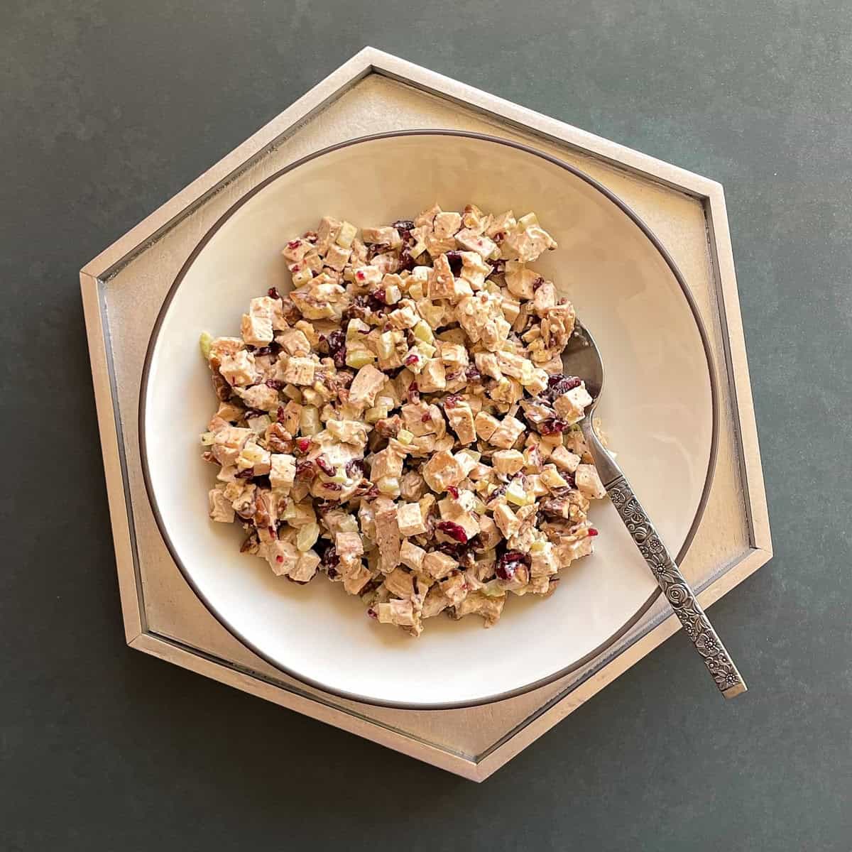 bowl of chicken salad with cranberries, pecans, and chopped celery and a metal spoon.