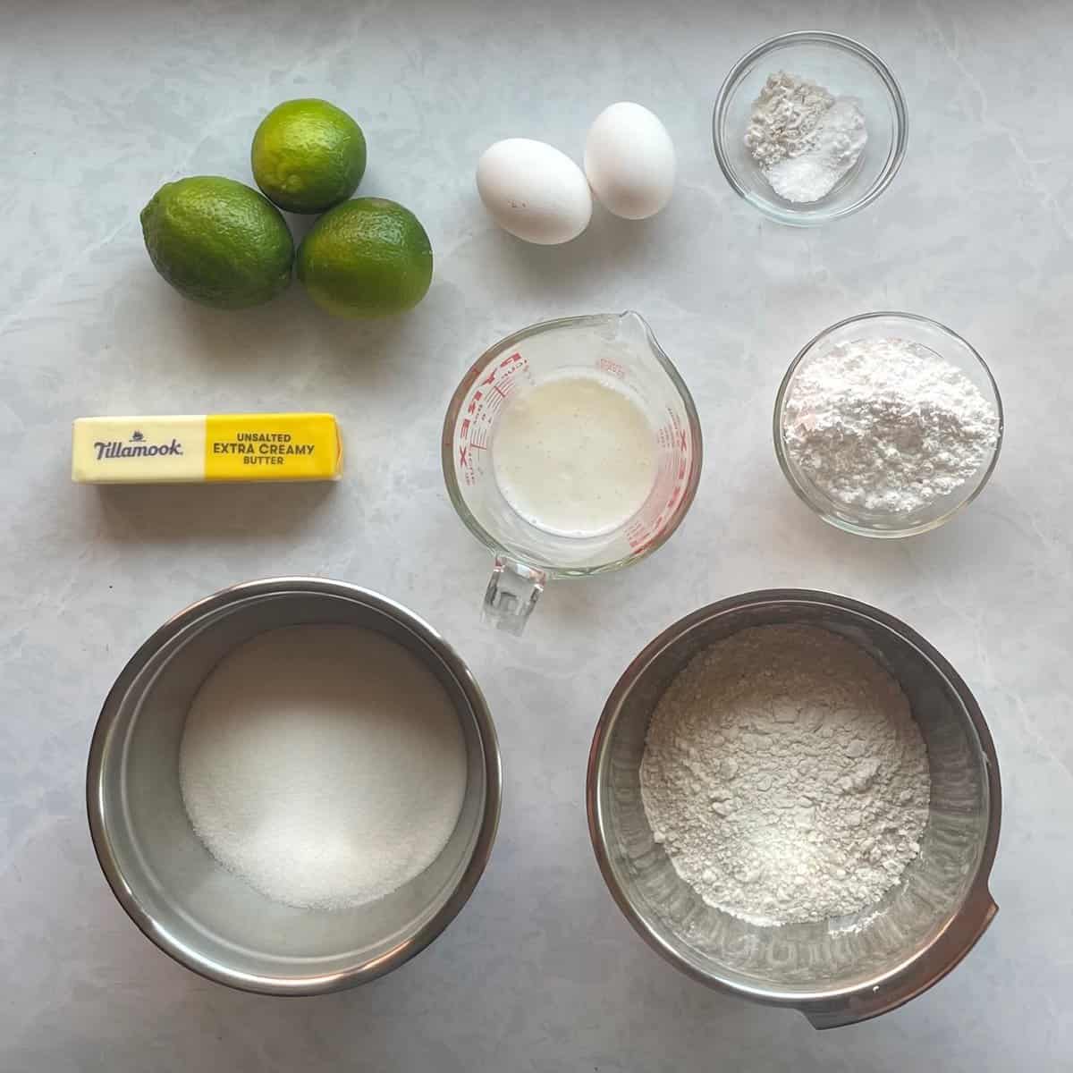 lime, butter, eggs, flour, sugar, salt, baking powder and soda on a countertop.