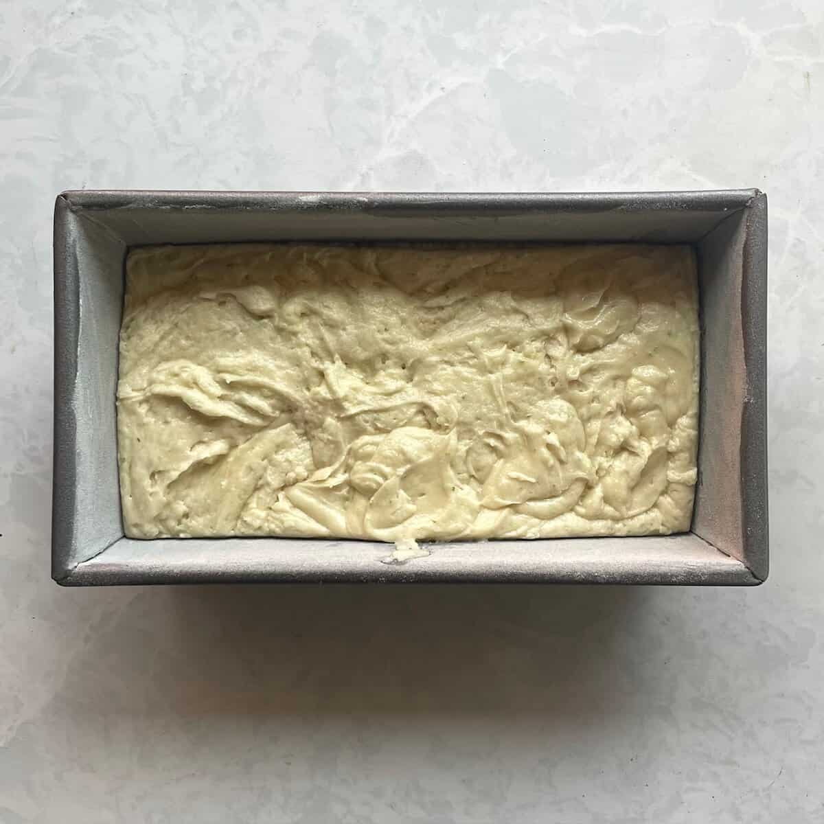 unbaked loaf cake batter flecked with lime zest in a loaf pan.