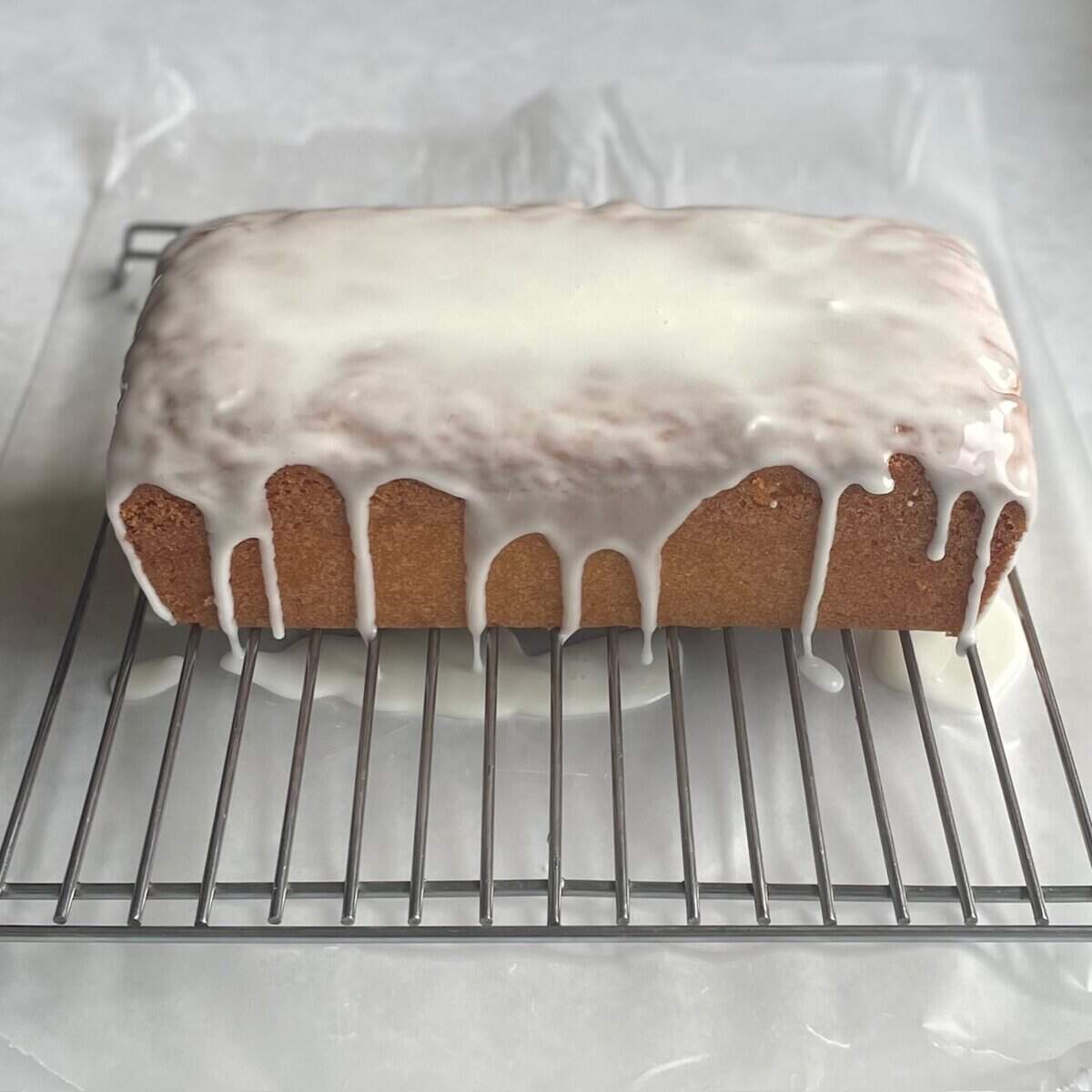 loaf cake with drizzle glaze dripping down the side on a cooling rack over waxed paper.