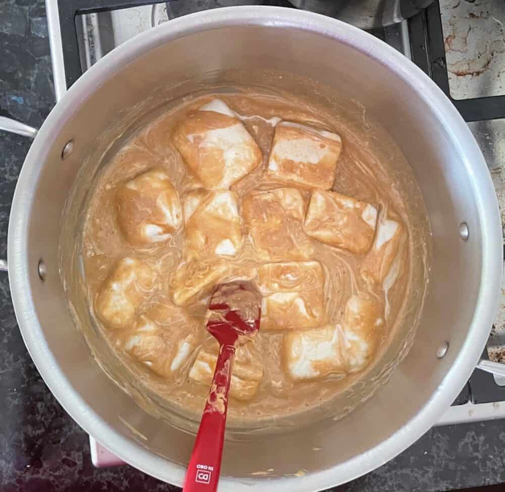 marshmallows melting in a pan of melted peanut butter colored liquid.