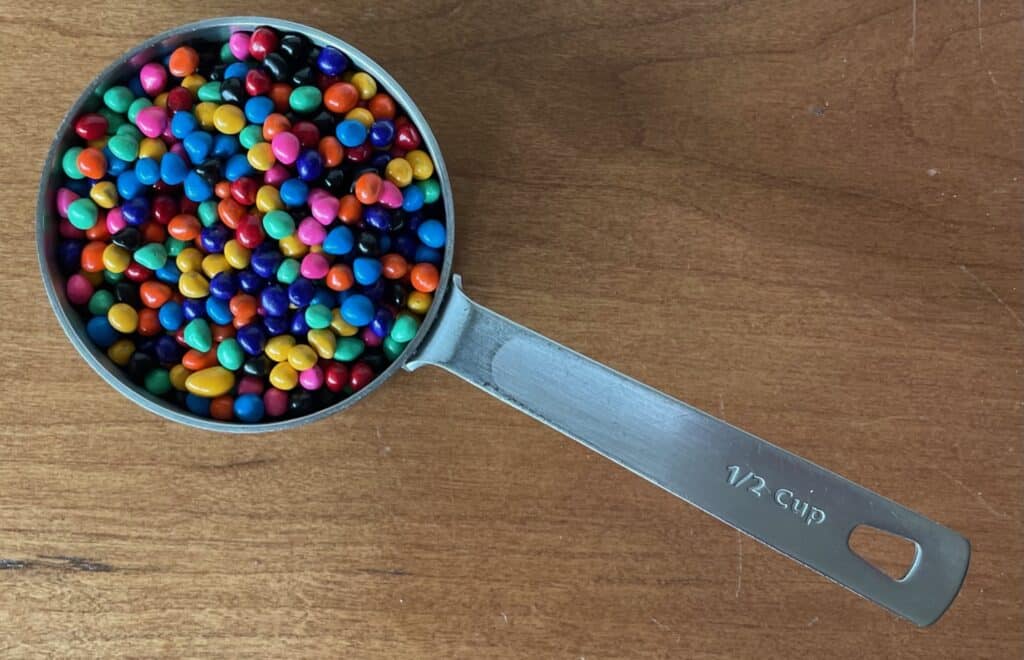 a measuring cup filled with rainbow chip sprinkles.