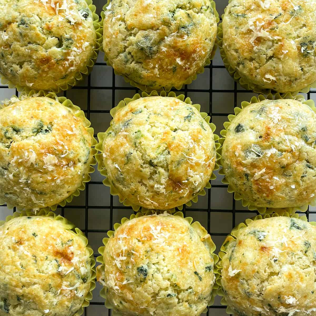 nine muffins on a cooling rack with flecks of spinach, feta, and Parmesan.