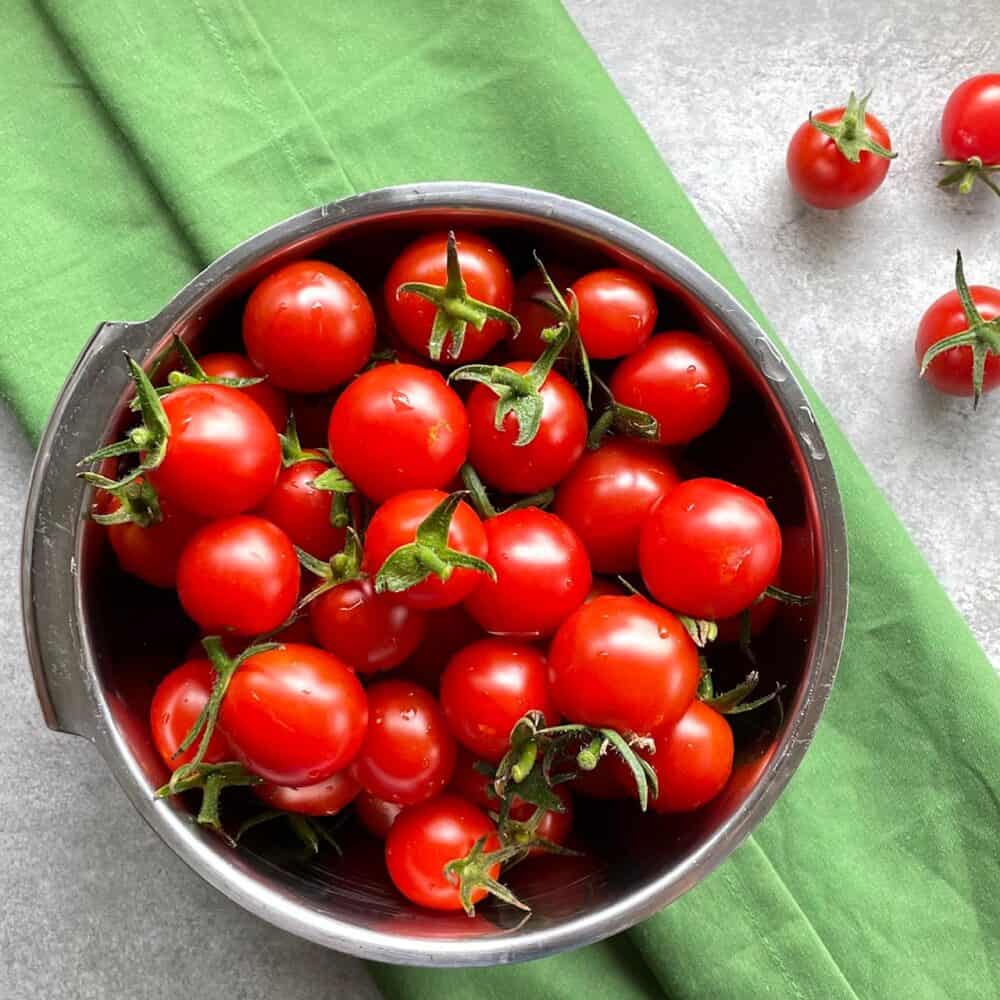 a bowl full of perfectly ripe cherry tomatoes on a green cloth.