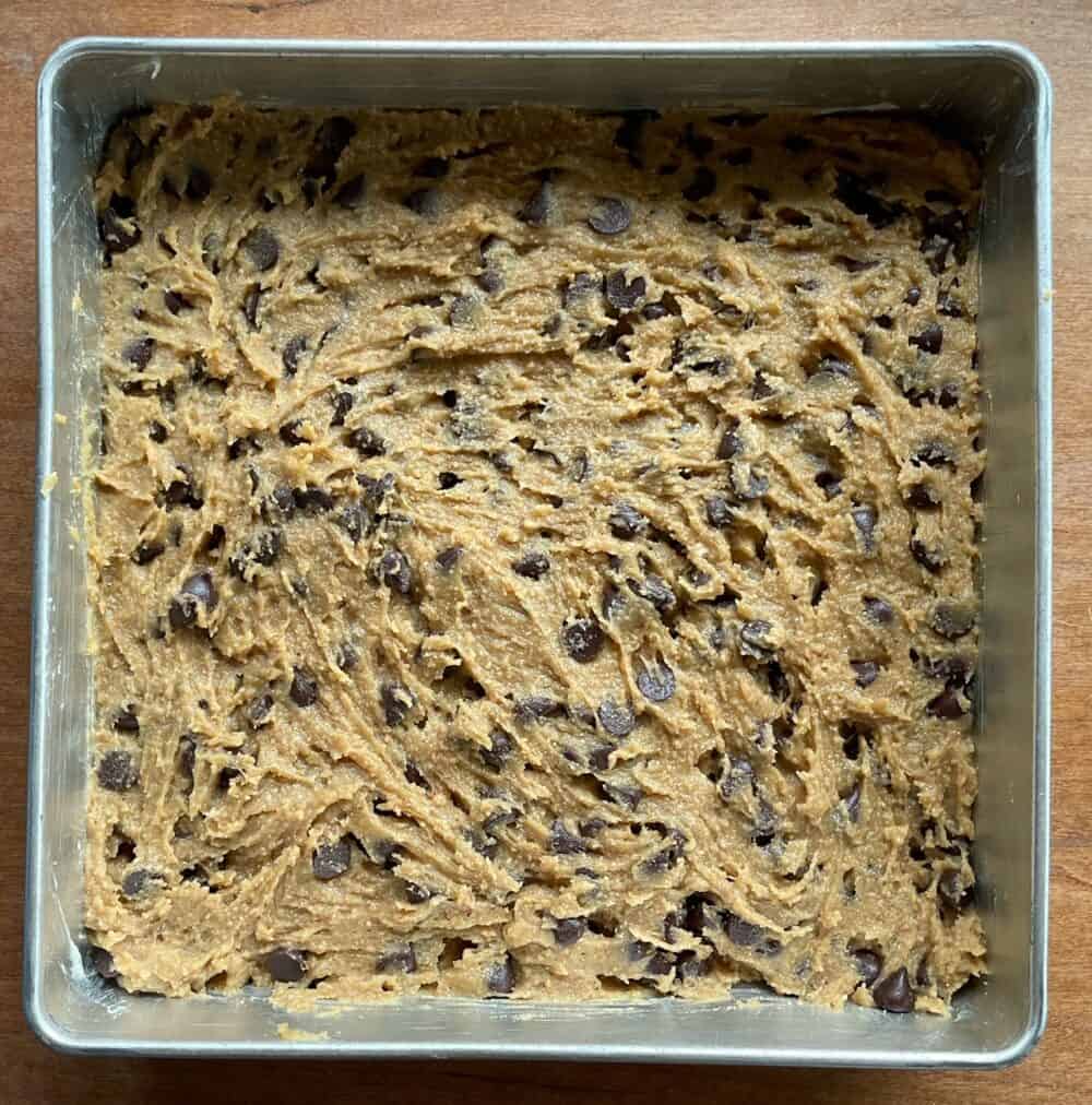 unbaked chocolate chip cookie bar batter in a greased square pan.
