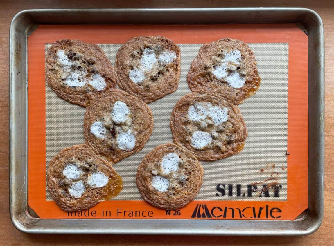 flattened smores cookies with melted marshmallows on a baking sheet.