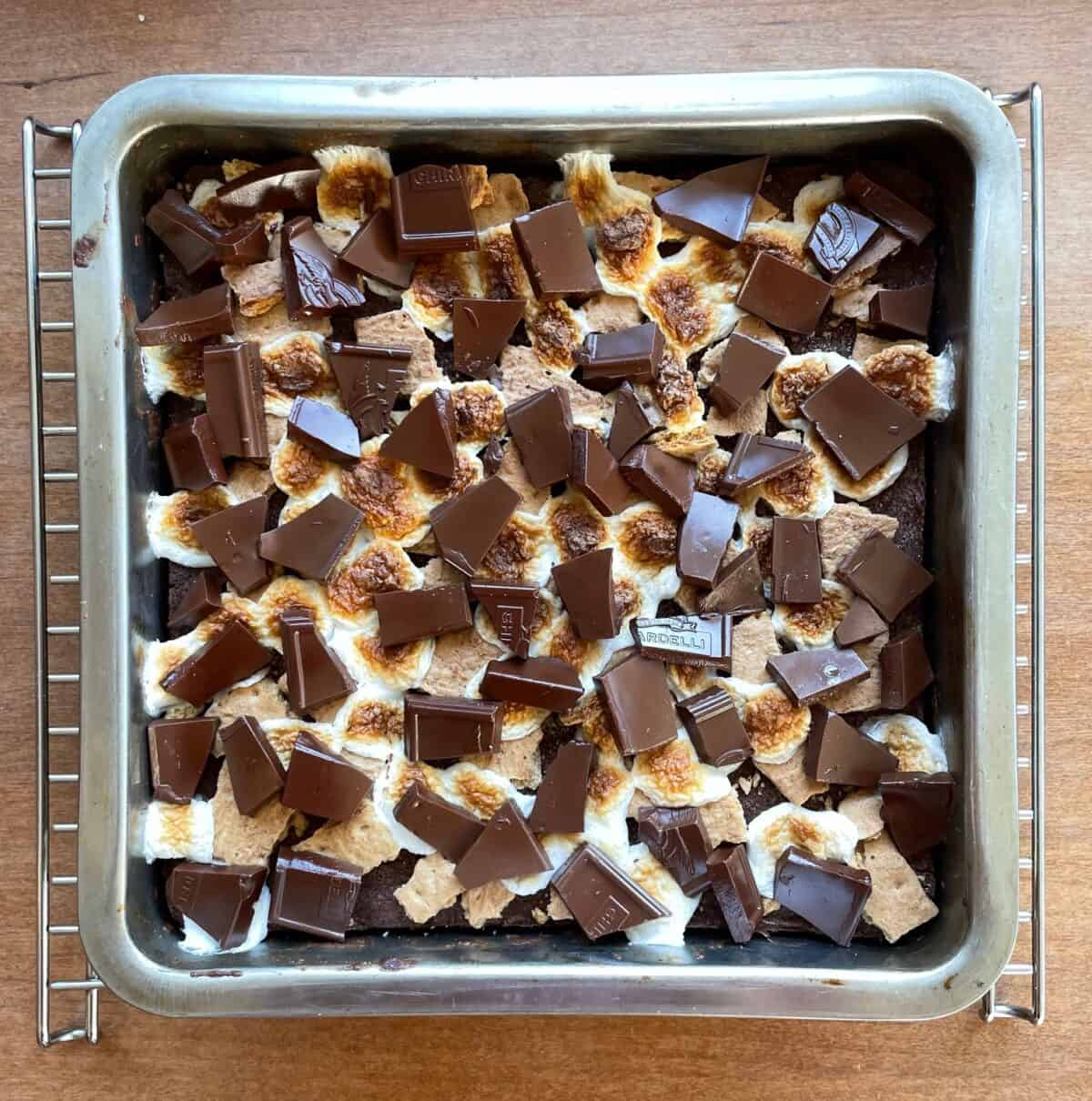 pan of brownies topped with graham crackers, chocolate bars pieces, and toasted marshmallows.
