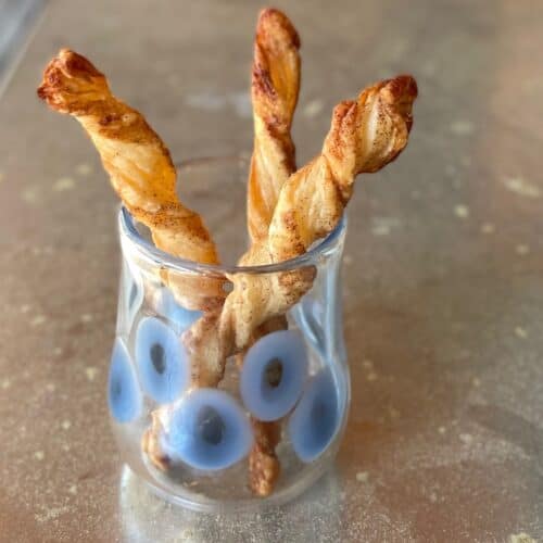 three puff pastry cinnamon twists standing upright in a glass.