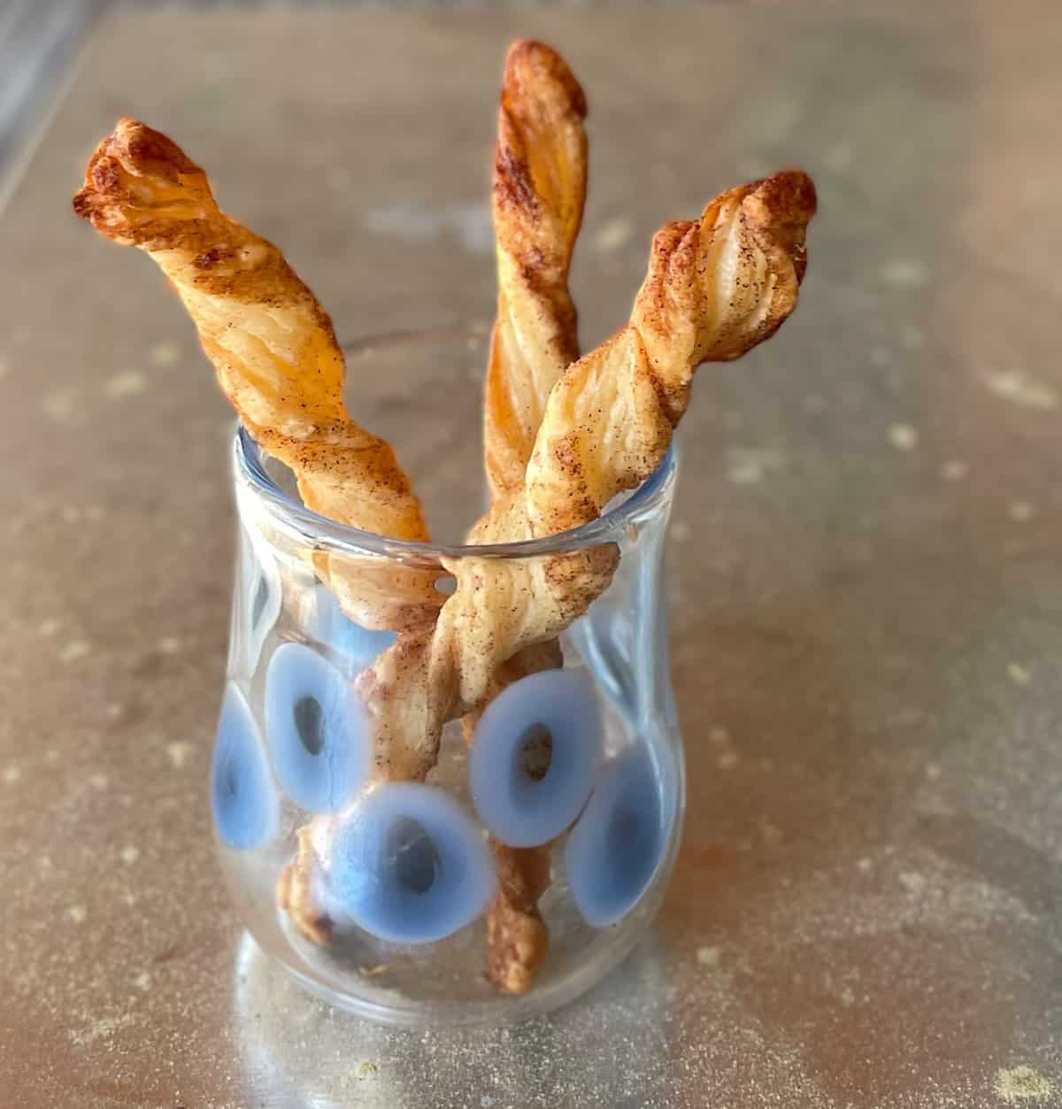 three puff pastry cinnamon twists standing upright in a glass.