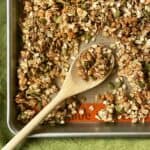 a wooden spoon scooping pumpkin seed granola on a baking sheet