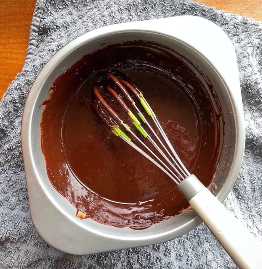 a bowl of melted chocolate filling with a whisk.