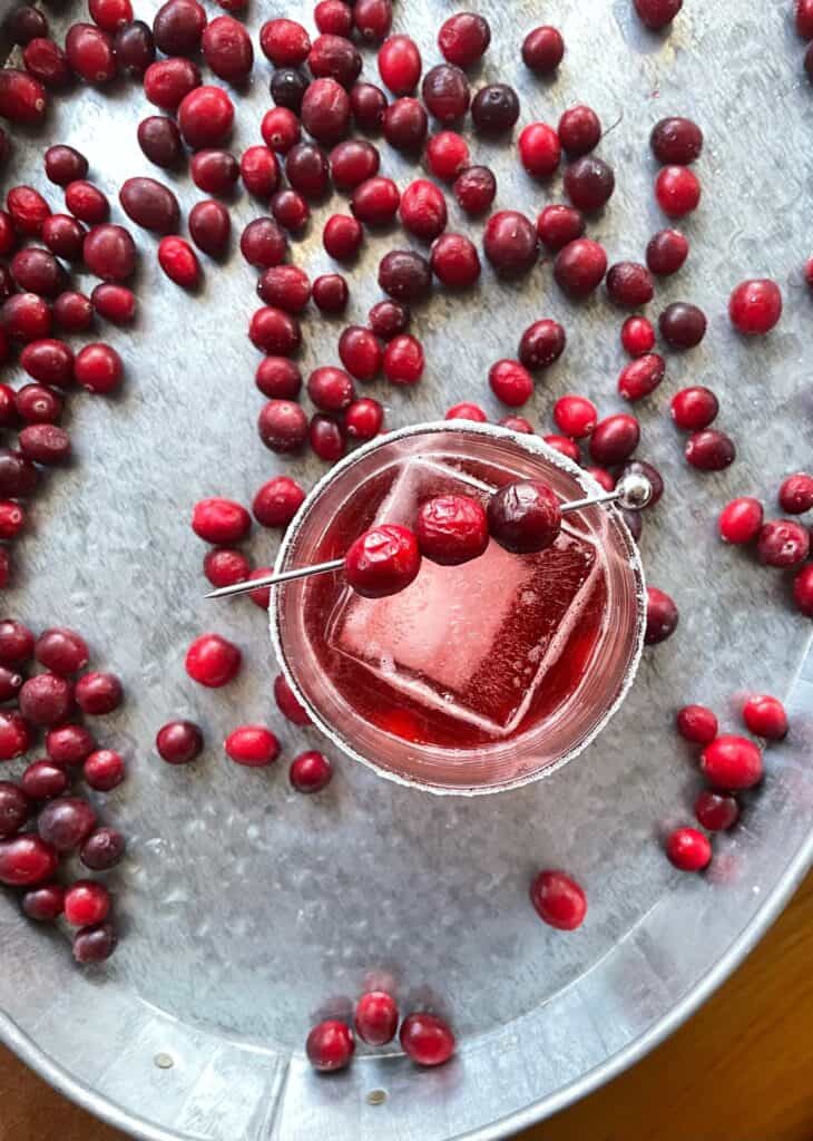 a cranberry negroni in a low ball glass on a tray filled with fresh cranberries.