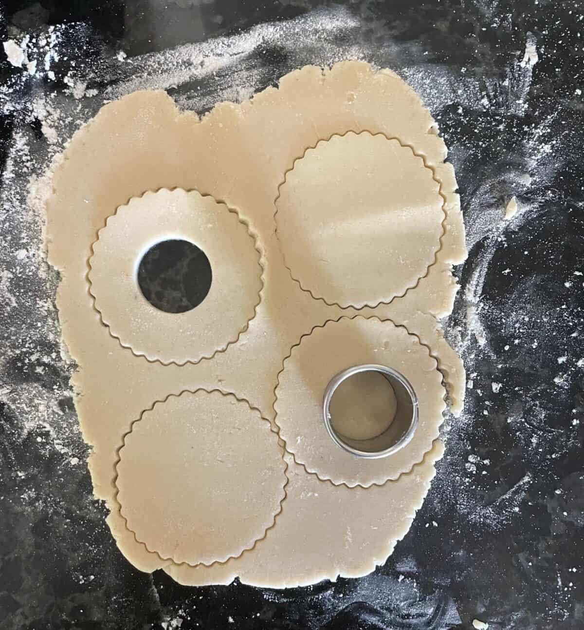rolled out cookie dough with fluted cookie cut outs, two of which have cut out centers.