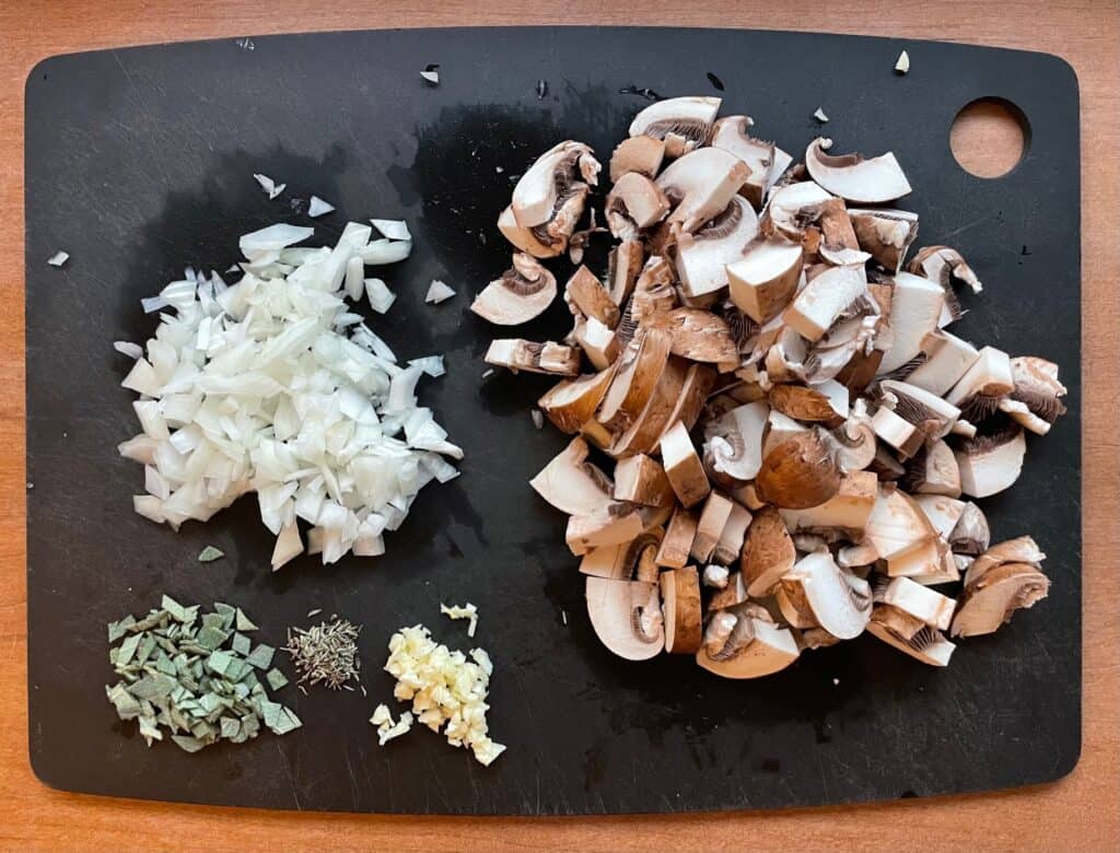 a cutting board with chopped onion, mushrooms, garlic, sage, and dried thyme.