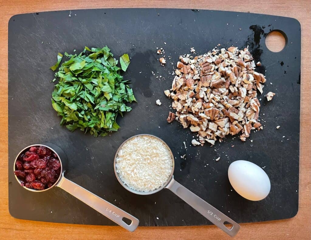 cutting board with chopped parsley, toasted pecans, dried cranberries, panko, and an egg.