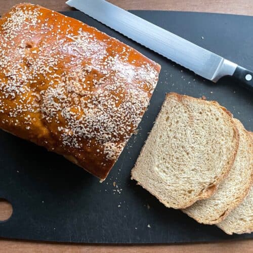 a sliced loaf of pretzel bread on a cutting board with a bread knife.