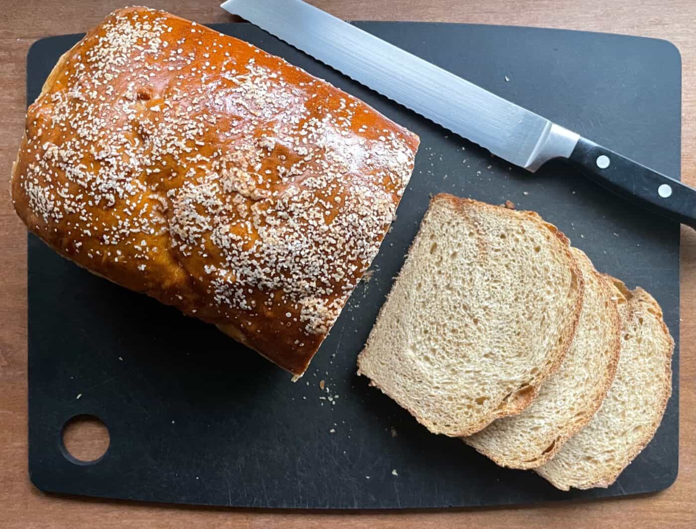 a sliced loaf of pretzel bread on a cutting board with a bread knife.