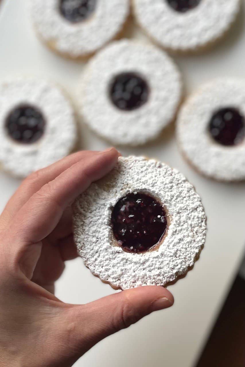a hand holding a cookie with other Linzer cookies in the background.