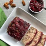 a cranberry pecan and mushroom turkey meatloaf on a plate with cranberry sauce glaze and pecans.