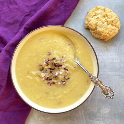 creamy potato soup topped with purple and green onions with a spoon and biscuit.
