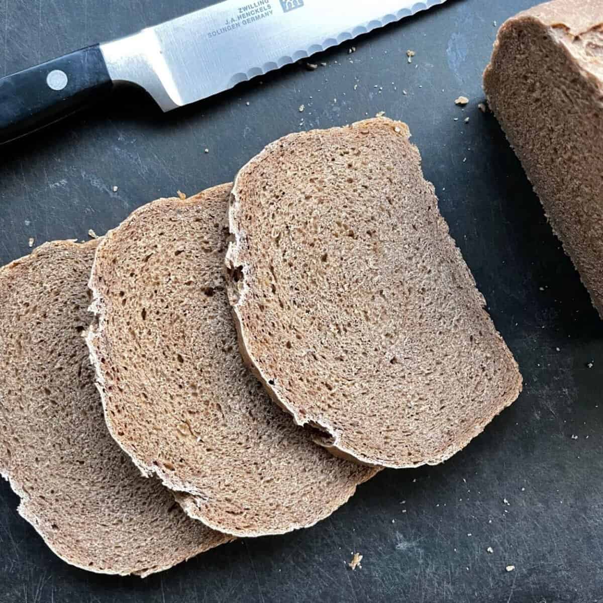 three slices of Russian rye sandwich bread on a cutting board with a bread knife.