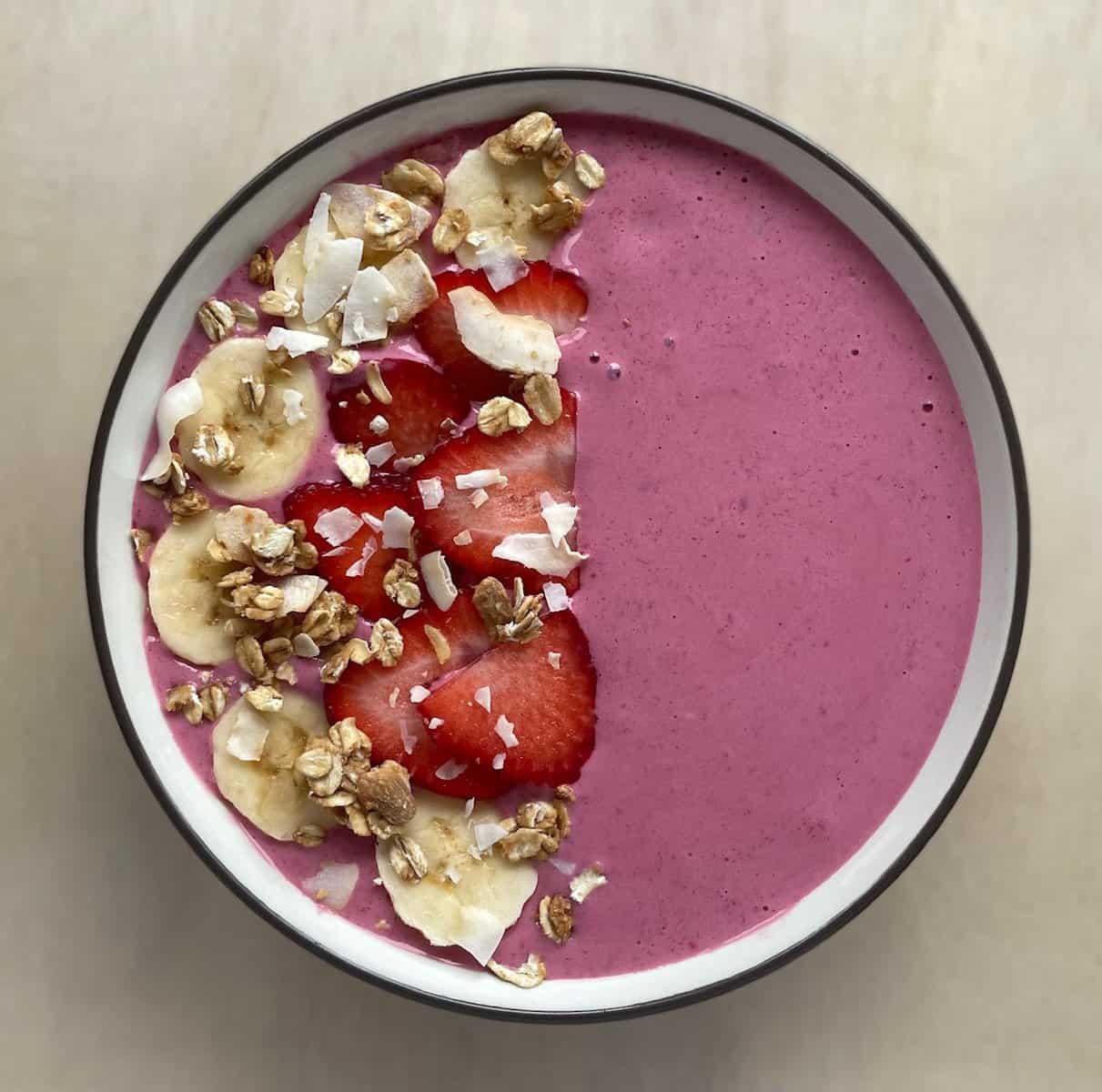 a pink smoothie bowl topped with fresh fruit and homemade granola