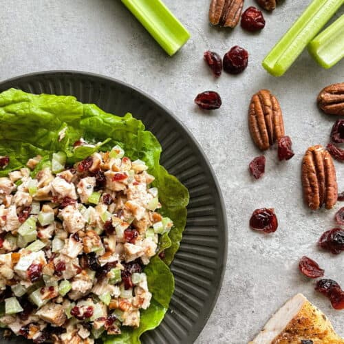 a plate of cranberry chicken salad surrounded by celery, cranberries, pecans, and chicken.
