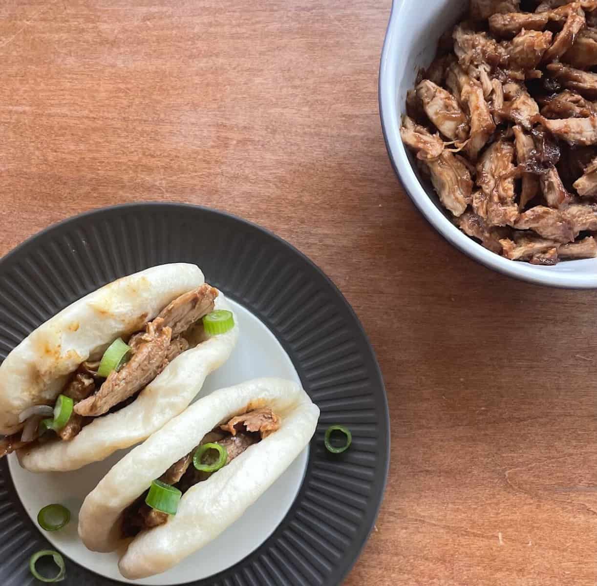 a bowl of pulled duck breast and a plate with steamed duck bao 