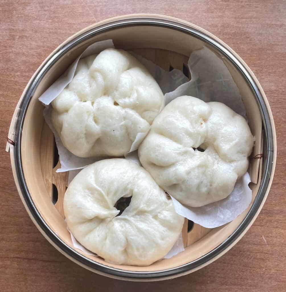 three steamed duck bao filled with pulled duck and green onions.