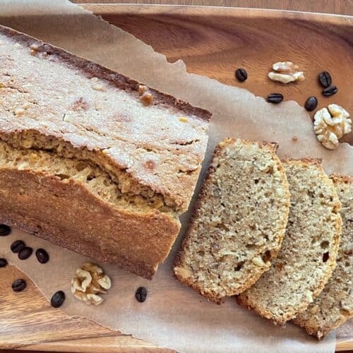 coffee and walnut cake cut into slices on parchment with walnuts and coffee beans.