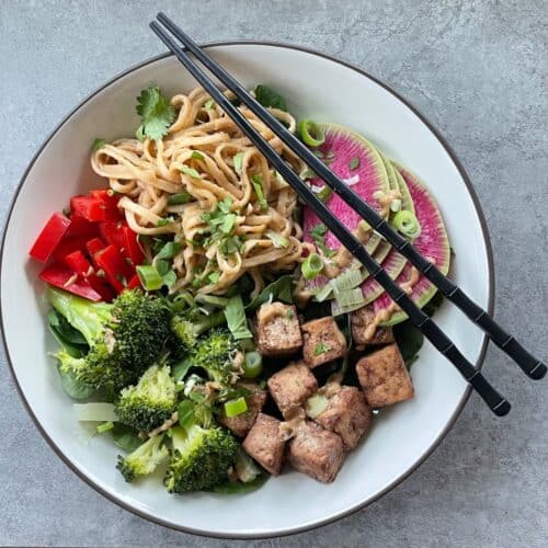 a bowl with tofu, peanut sauce noodles, broccoli, and other vegetables.
