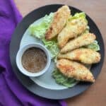 five baked coconut panko chicken tenders on a plate with honey mustard sauce.