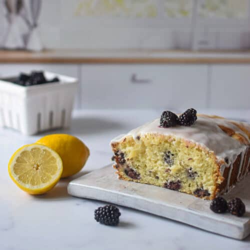 sliced blackberry lemon bread on the counter with blackberries and cut lemon.